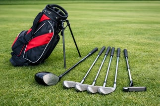Beginner golf club set including used driver, irons, putter, and golf bag arranged on grass